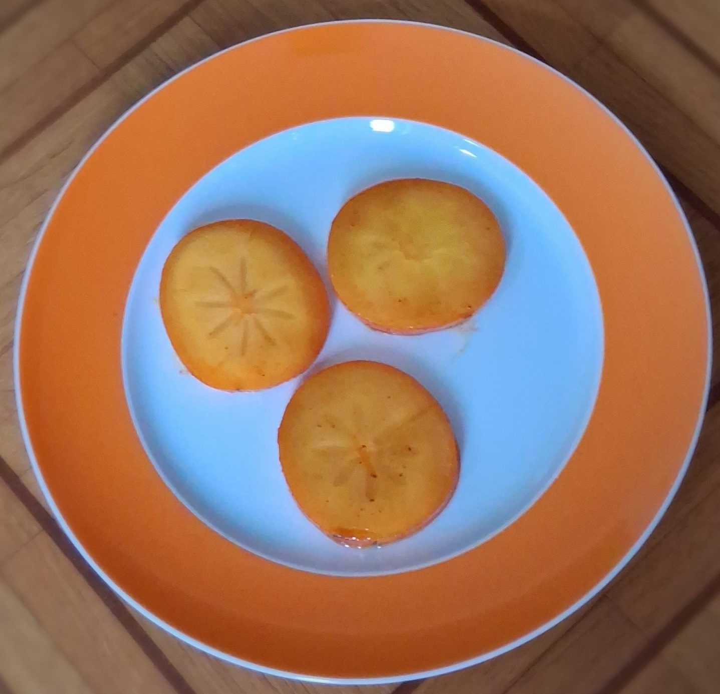 Gebratene Khakischeiben auf einem Teller mit orangenem rand