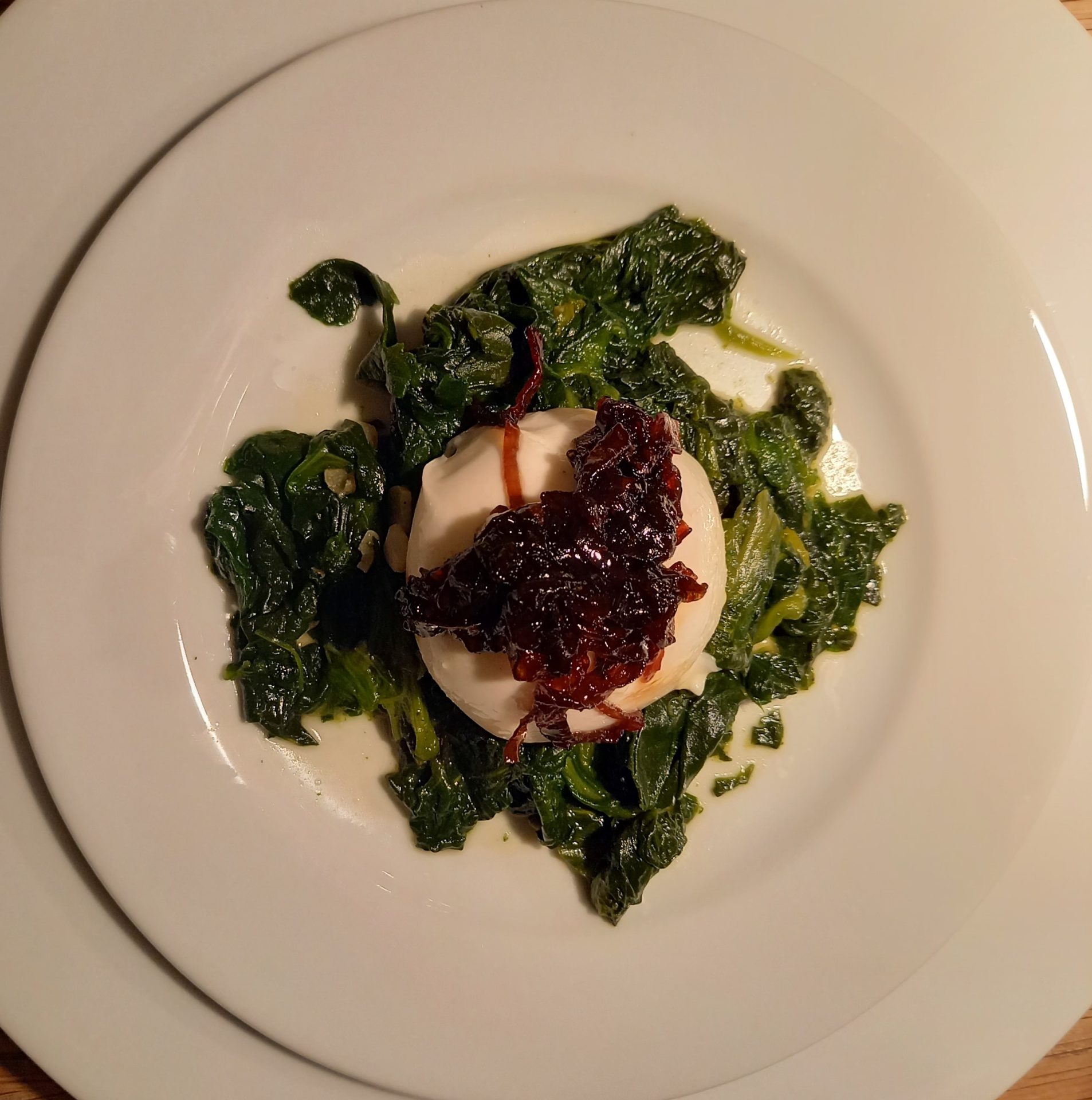 Burrata am Stück mit einer Haube konfierten Schalotten auf einem Spinatbett